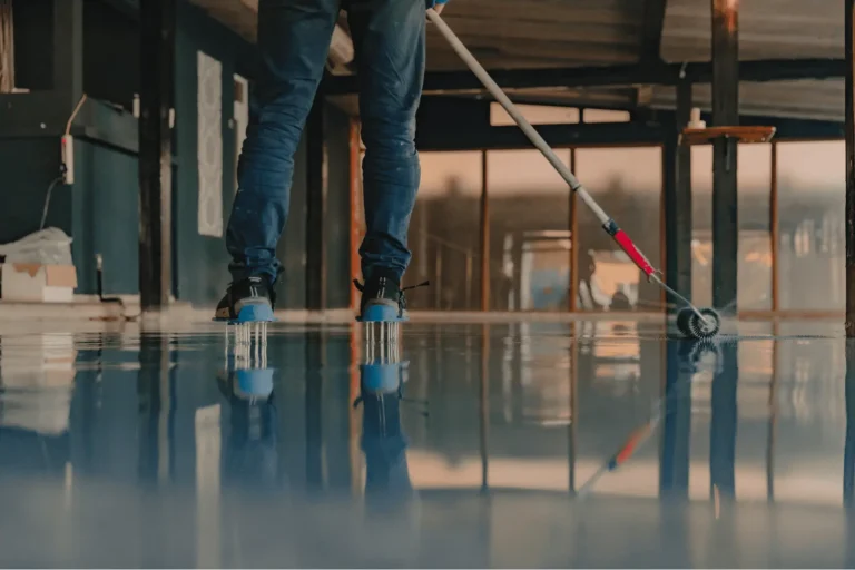 Installer using spiked shoes and roller to apply epoxy floor coating.