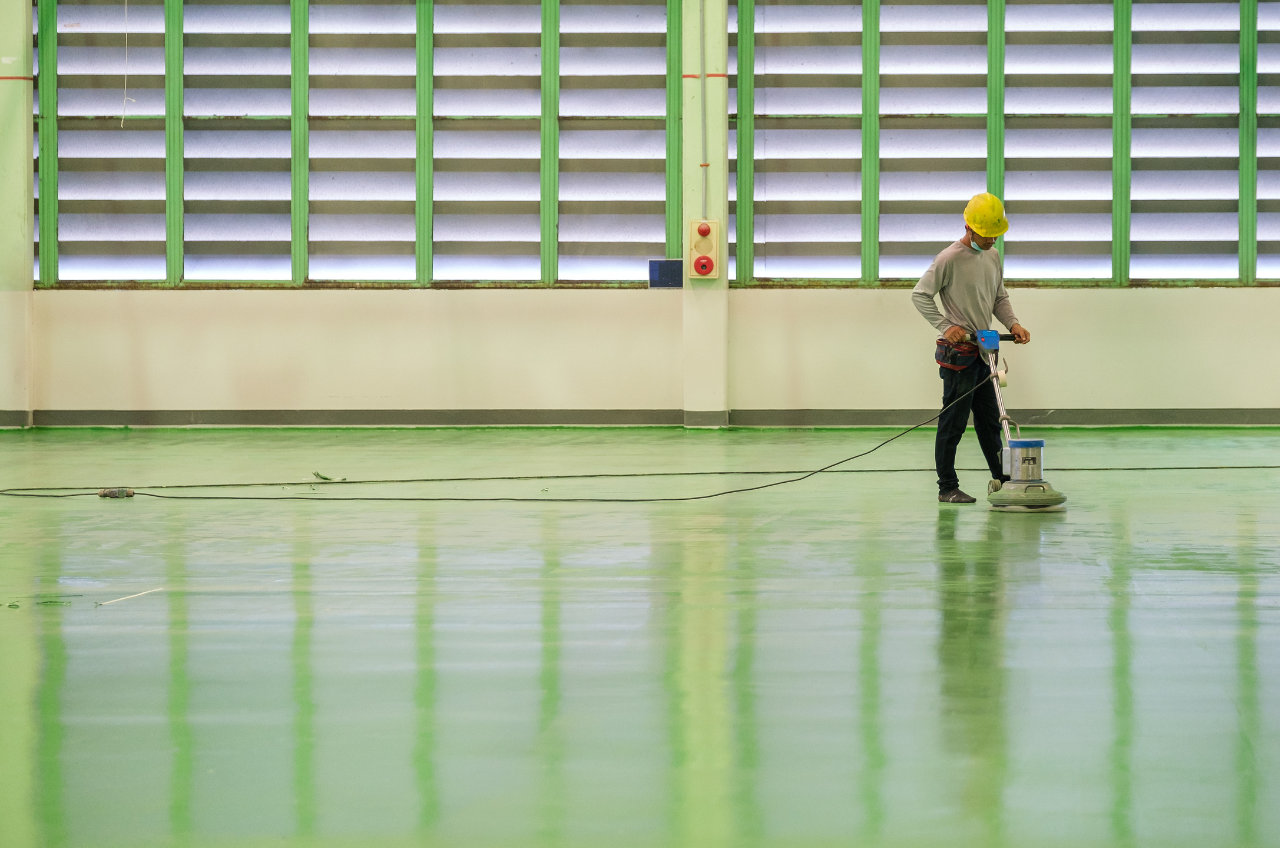 Worker using a floor buffer machine on a newly finished green epoxy floor in an industrial warehouse.