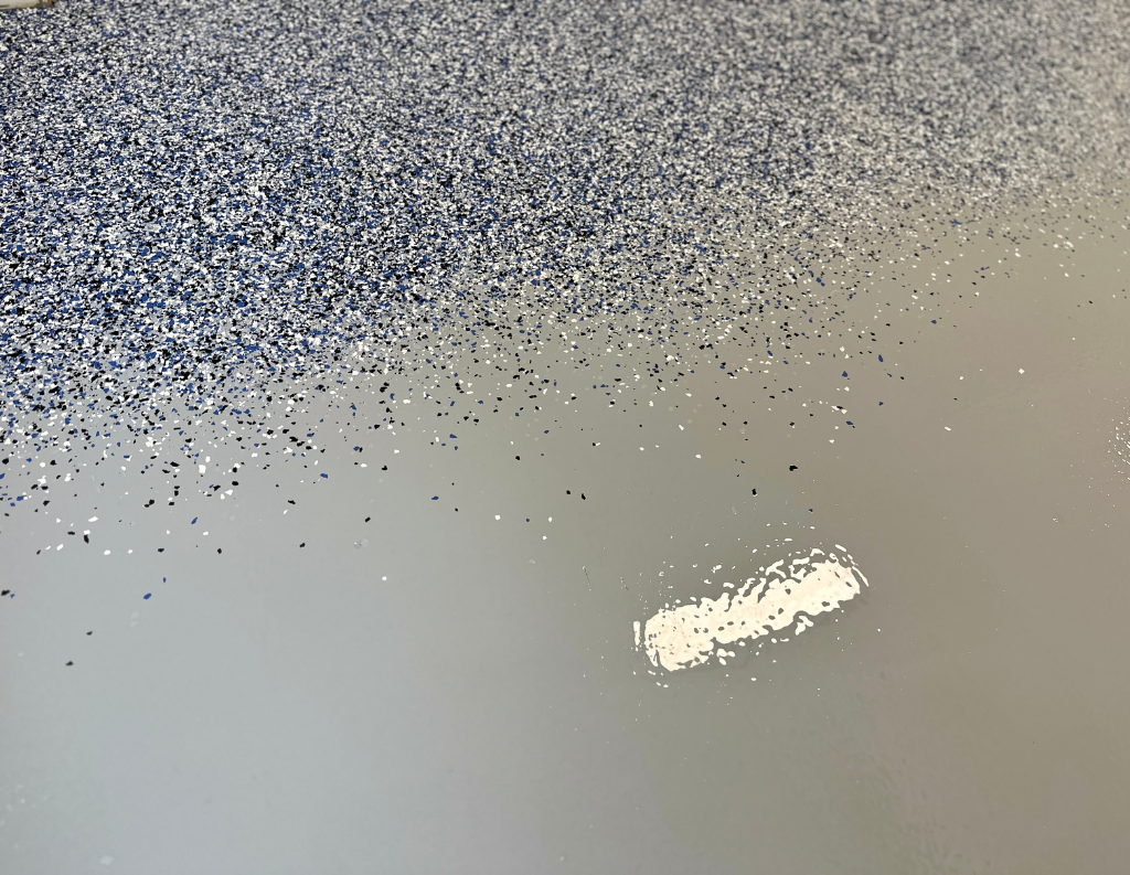 Close-up of decorative flake being broadcast onto wet rubberized urethane