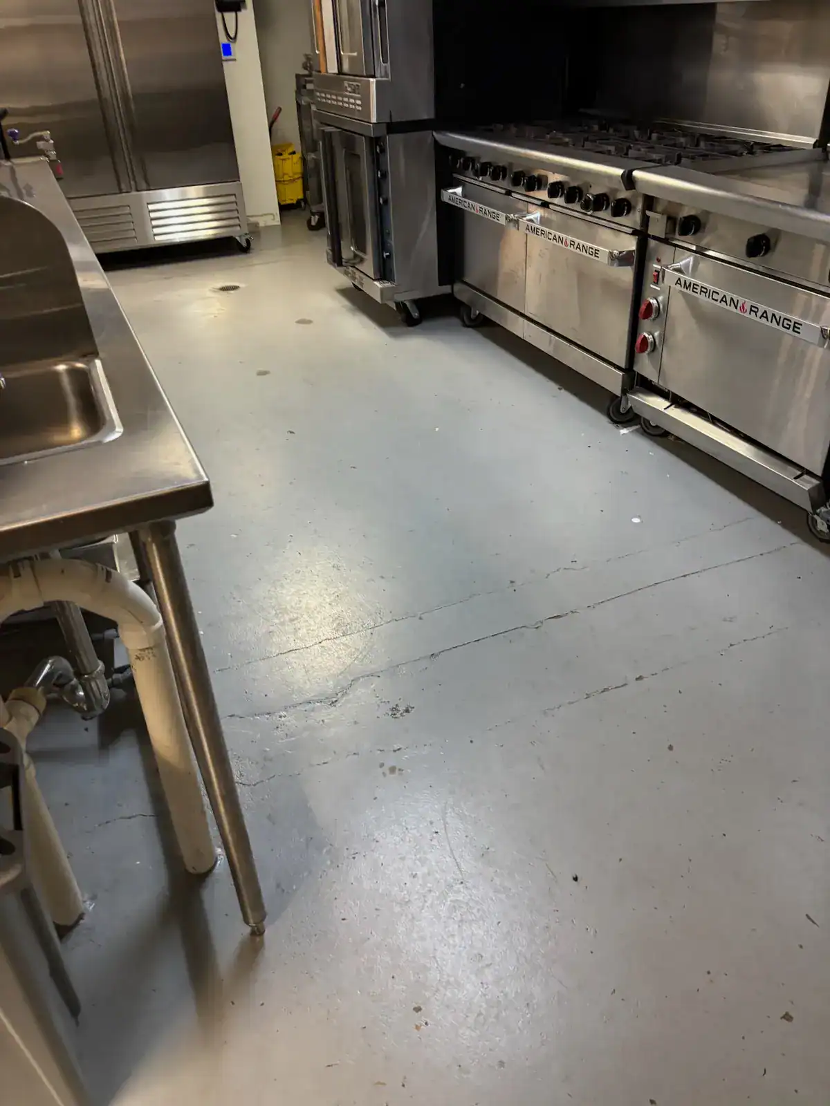 Cracks and worn areas in an older commercial kitchen floor before preparation